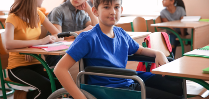 Niepełnosprawny chłopiec na wózku inwalidzkim siedzi szkolnej klasie.