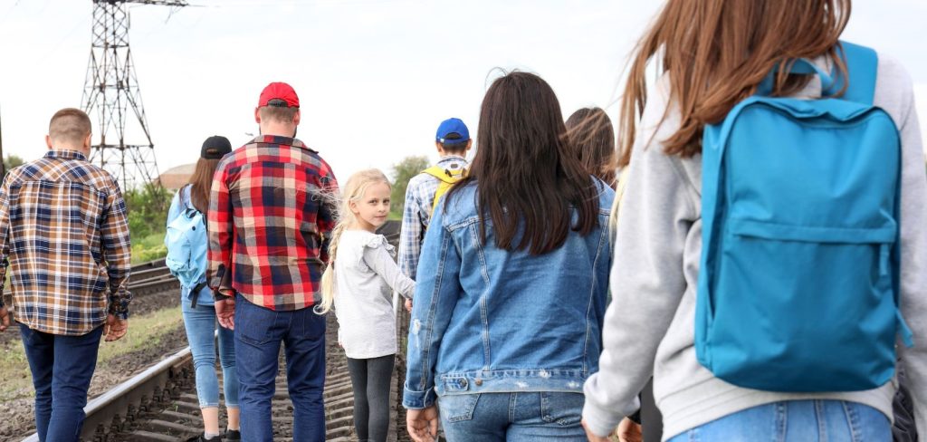 Grupa osób, która porusza się obok torów i jest odwrócona plecamy