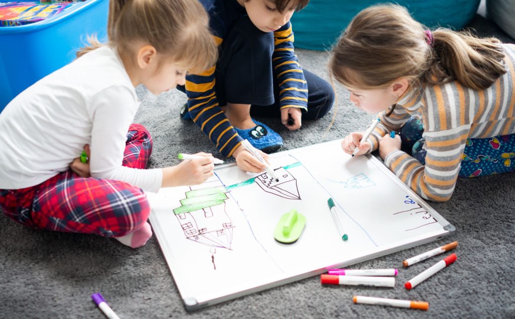 Trójka dzieci siedzi na dywanie i rysuje na kartce papieru