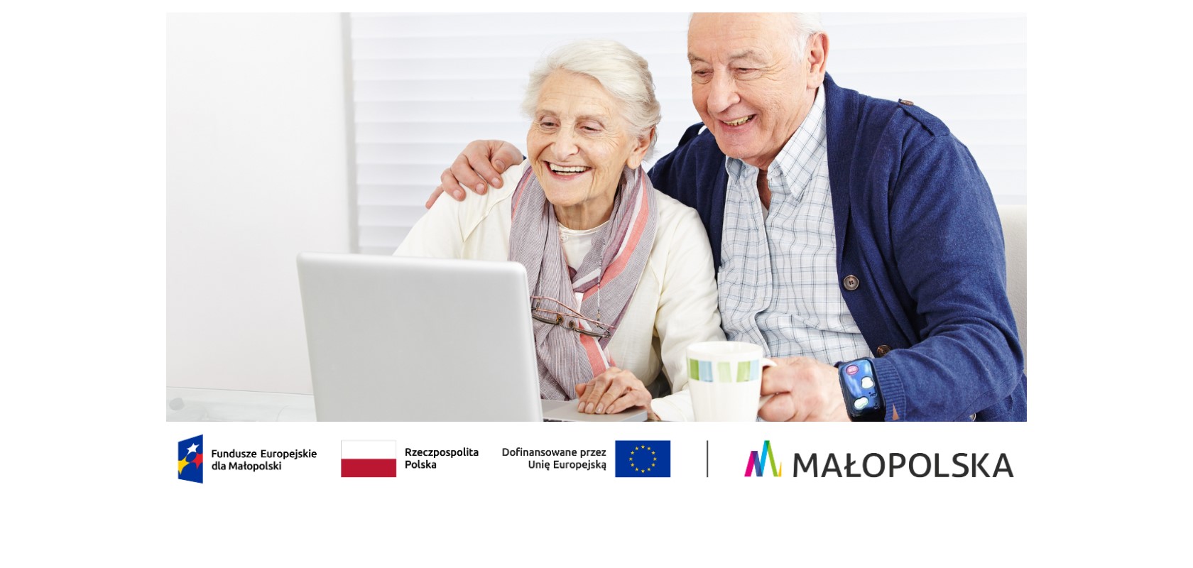 Starszy mężczyzna jedną ręką obejmuje starszą kobietę, a w drugiej ma założony zegarek z projektu Tele Anioł i jednocześnie trzyma kubek. Oboje uśmiechnięci siedzą przed laptopem wpatrując się w niego.