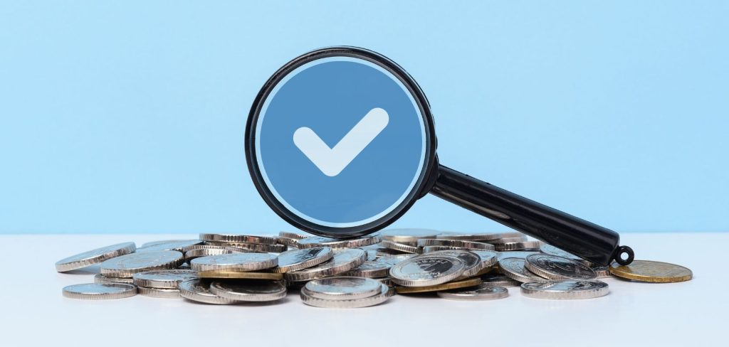 monety leżące na stole, szkło powiększające i znak zaznaczenia w kole