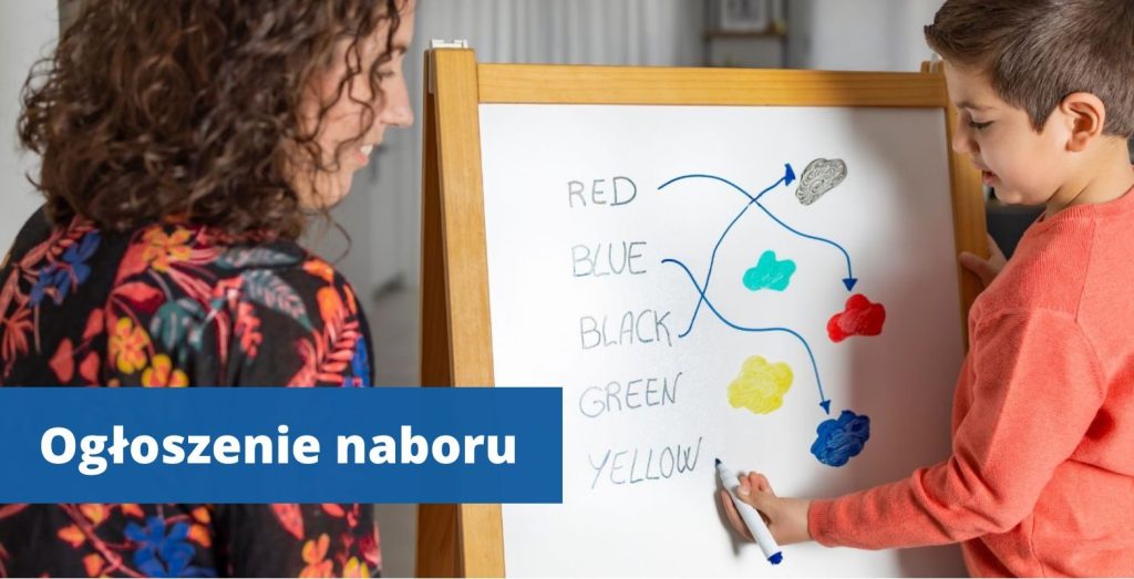 Przy tablicy stoi mały chłopiec i rysuje a obok nauczycielka