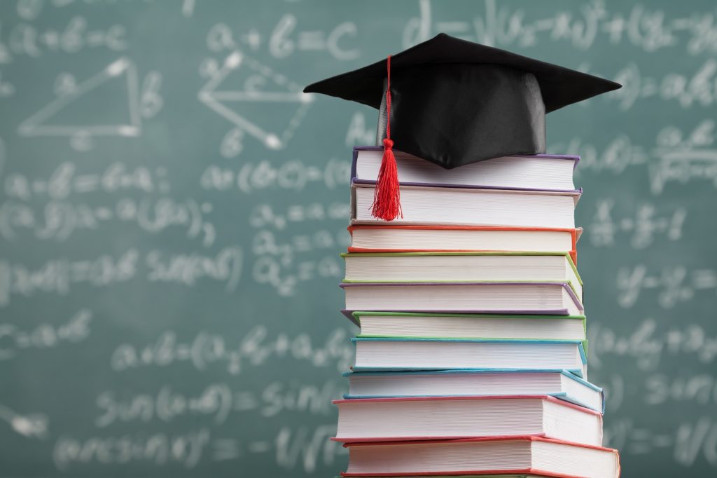 Stos ksiązek a na nim czapka studencka