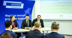 Przy stole dla prezentujących siedzi min Marszałek Województwa Małopolskiego Łukasz Smółka a na widowni ludzie