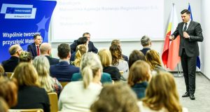 Przemawia Marszałek Województwa Małopolskiego Łukasz Smółka a na widowni siedzi pełna sala ludzi 